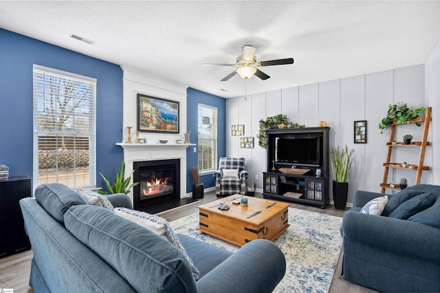 living room with a textured ceiling, ceiling fan, a fireplace with flush hearth, wood finished floors, and visible vents