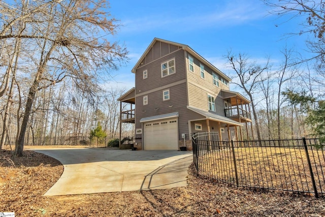 view of side of property with concrete driveway, an attached garage, board and batten siding, fence, and a balcony