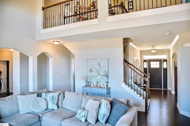 living room featuring baseboards, dark wood finished floors, a towering ceiling, ornamental molding, and stairs