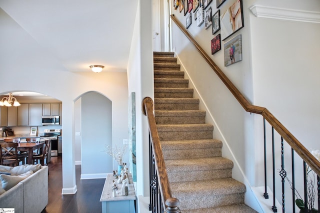 stairway with arched walkways, a notable chandelier, wood finished floors, and baseboards