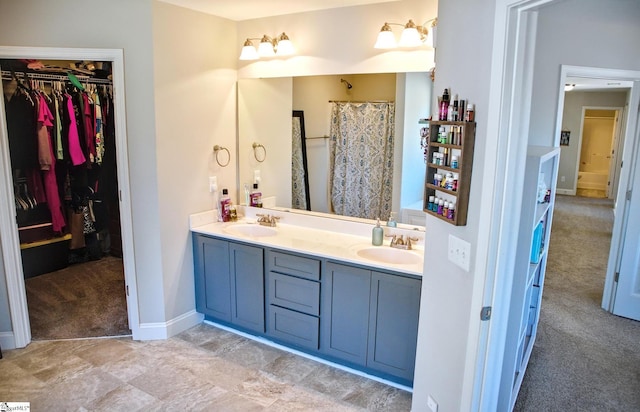 bathroom with double vanity, a sink, a walk in closet, and baseboards