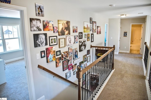 corridor featuring carpet, baseboards, and an upstairs landing