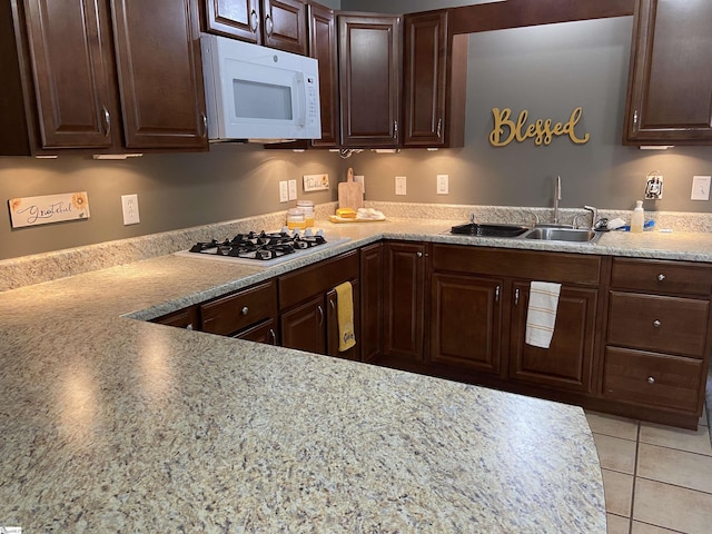 kitchen featuring white appliances, light tile patterned flooring, a sink, and dark brown cabinetry