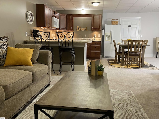 living room featuring light carpet, a drop ceiling, and baseboards