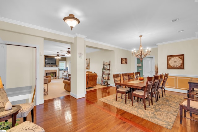 dining area with crown molding, a fireplace, wood finished floors, and ceiling fan with notable chandelier