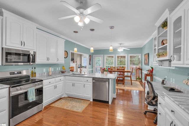 kitchen featuring light wood-style flooring, stainless steel appliances, a peninsula, white cabinets, and ornamental molding