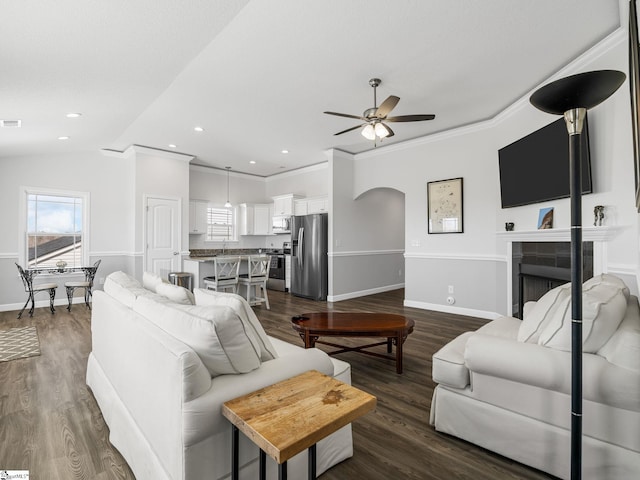living area featuring arched walkways, dark wood-style flooring, a fireplace, crown molding, and baseboards