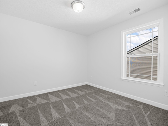 spare room with dark colored carpet, visible vents, and baseboards