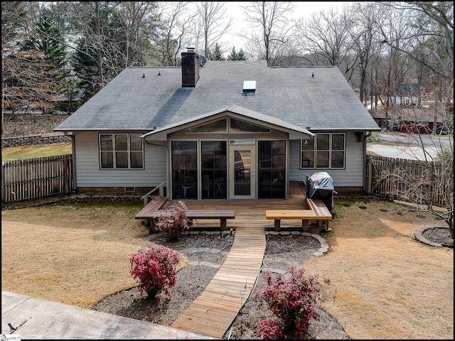 back of house featuring a fenced backyard, a sunroom, roof with shingles, a wooden deck, and a chimney