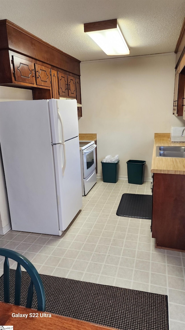 kitchen with a textured ceiling, light tile patterned floors, white appliances, a sink, and light countertops