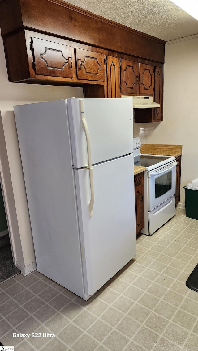 kitchen with a textured ceiling, light countertops, white appliances, and under cabinet range hood