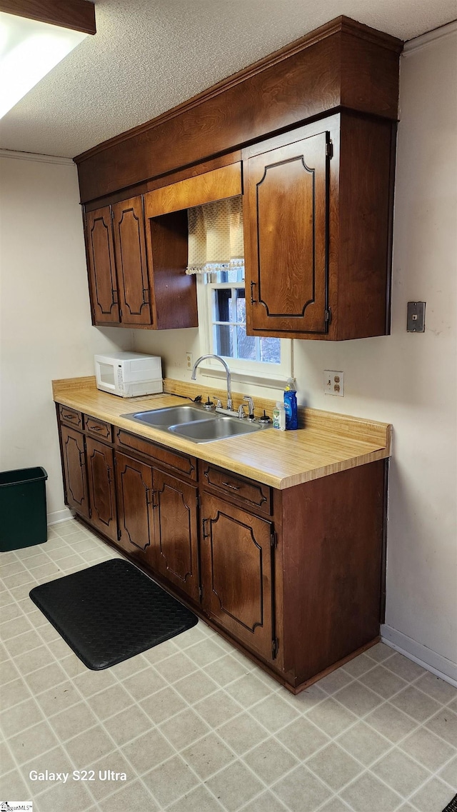 kitchen with light countertops, white microwave, a sink, a textured ceiling, and baseboards