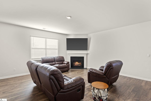 living room with a warm lit fireplace, dark wood finished floors, visible vents, and baseboards