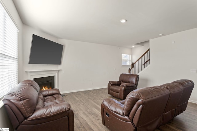 living area with stairs, wood finished floors, a glass covered fireplace, and baseboards