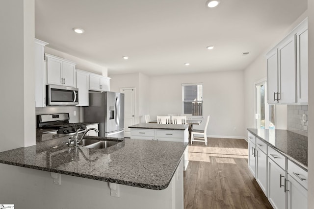 kitchen featuring dark wood-style floors, stainless steel appliances, white cabinets, a sink, and a peninsula