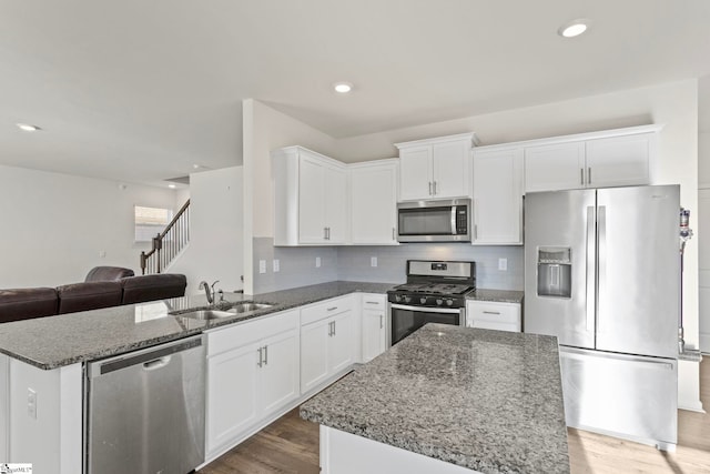 kitchen featuring dark stone counters, appliances with stainless steel finishes, wood finished floors, and white cabinets