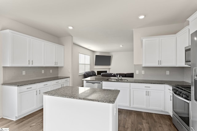 kitchen with dark wood-style flooring, a sink, white cabinets, open floor plan, and appliances with stainless steel finishes