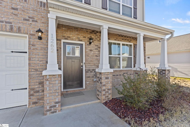 entrance to property with a garage, covered porch, and brick siding