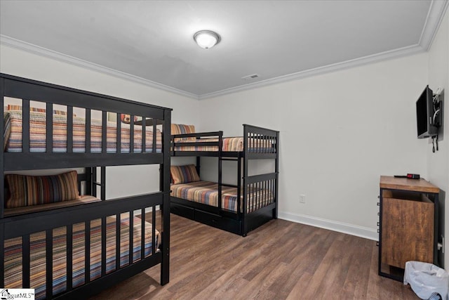 bedroom with ornamental molding, visible vents, baseboards, and wood finished floors