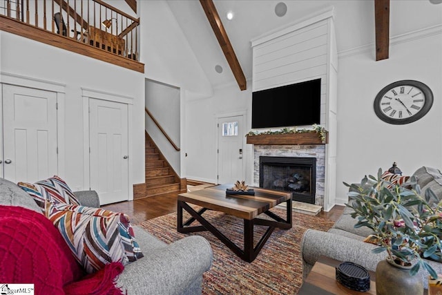 living room featuring beam ceiling, stairway, a stone fireplace, wood finished floors, and high vaulted ceiling