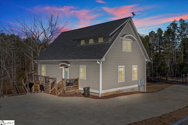 back of house at dusk with roof with shingles and a wooden deck