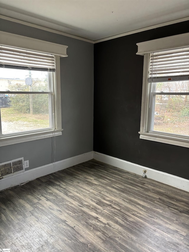 empty room with baseboards, wood finished floors, visible vents, and crown molding