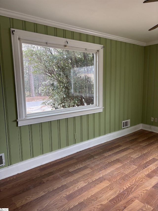 spare room with plenty of natural light, wood finished floors, visible vents, and baseboards