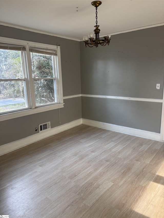 empty room with crown molding, visible vents, an inviting chandelier, light wood-style floors, and baseboards