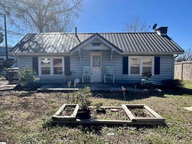 view of front of house featuring a vegetable garden, metal roof, a chimney, and fence