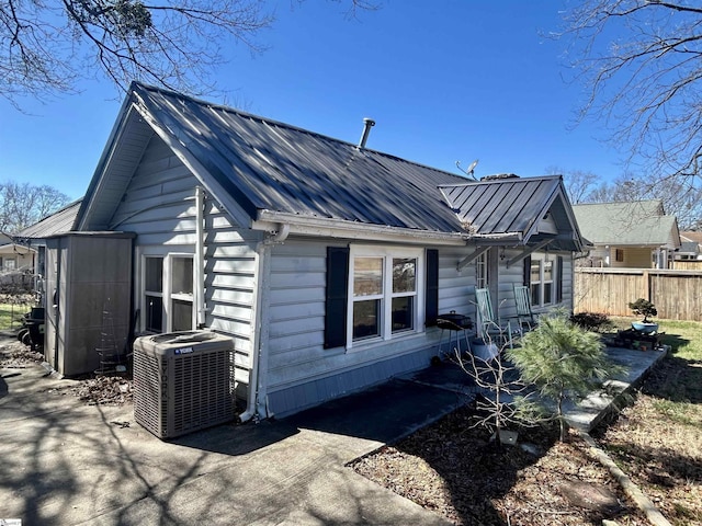 view of side of home with cooling unit, metal roof, and fence