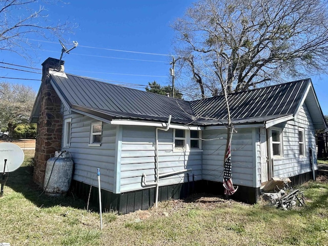 rear view of house featuring a chimney, metal roof, and a yard