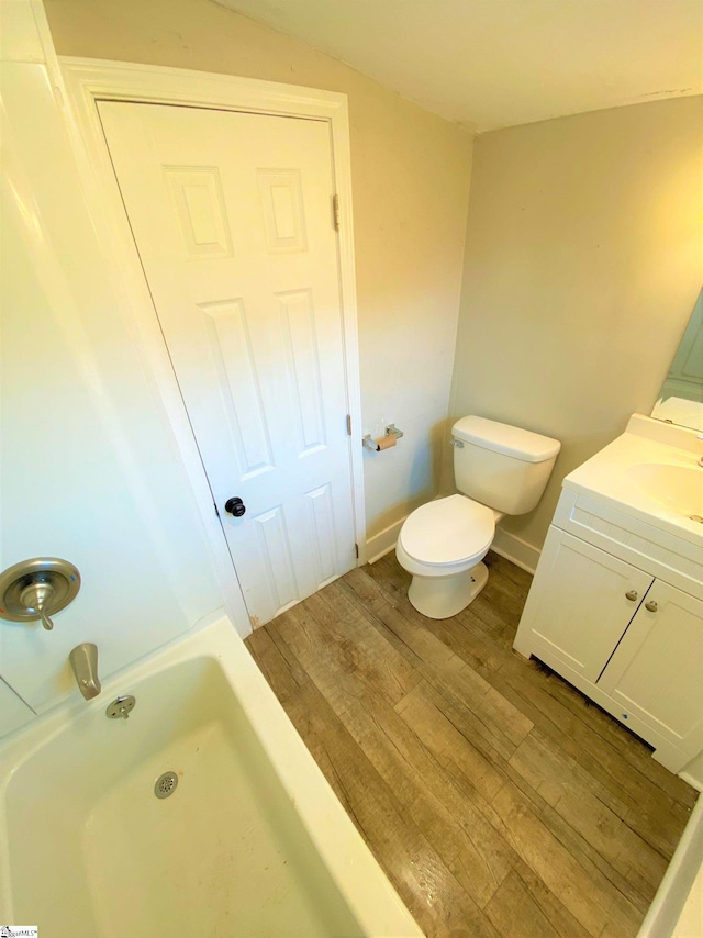 bathroom featuring toilet, wood finished floors, vanity, baseboards, and vaulted ceiling