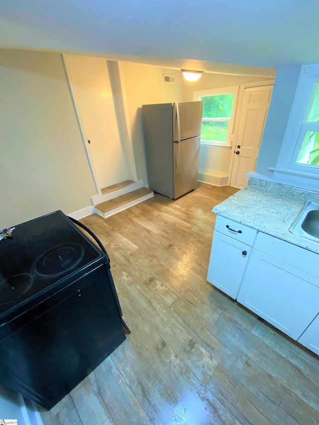 kitchen featuring electric range, light wood-style flooring, light stone counters, freestanding refrigerator, and white cabinetry