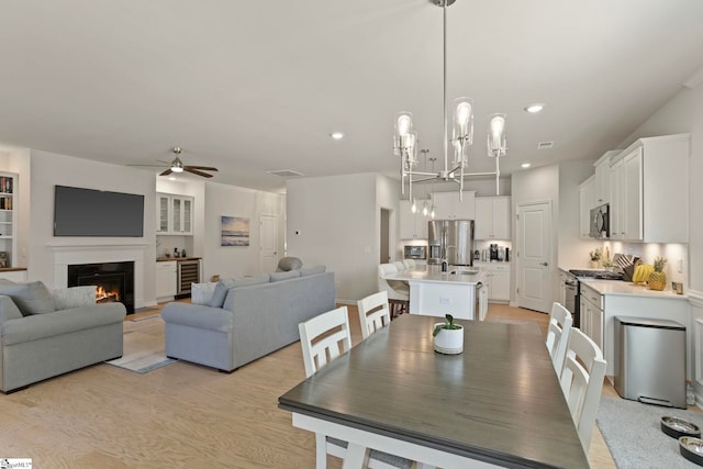 dining area with recessed lighting, a ceiling fan, a glass covered fireplace, light wood-type flooring, and beverage cooler