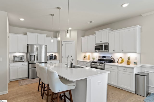 kitchen with light wood finished floors, stainless steel appliances, a kitchen island with sink, a sink, and a kitchen bar