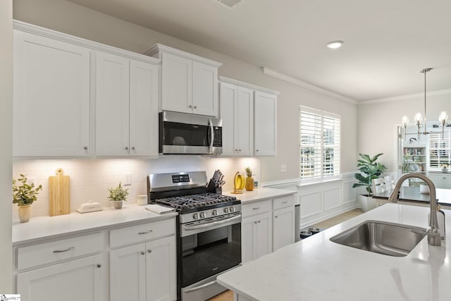 kitchen with a sink, white cabinets, light countertops, ornamental molding, and appliances with stainless steel finishes