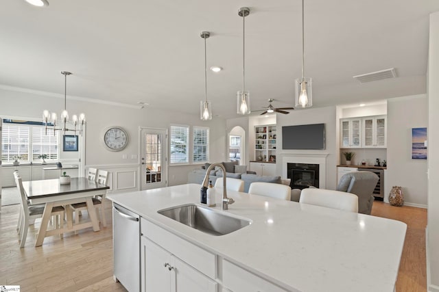 kitchen featuring a sink, visible vents, dishwasher, a glass covered fireplace, and a center island with sink