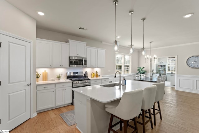 kitchen featuring a kitchen island with sink, stainless steel appliances, a sink, visible vents, and light wood finished floors