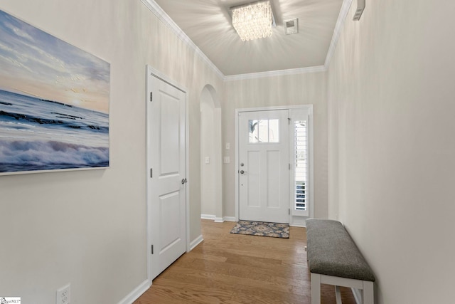 entryway featuring arched walkways, crown molding, visible vents, wood finished floors, and baseboards