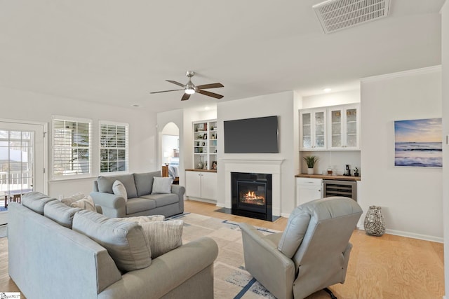 living area featuring light wood-style flooring, beverage cooler, a fireplace with flush hearth, visible vents, and baseboards