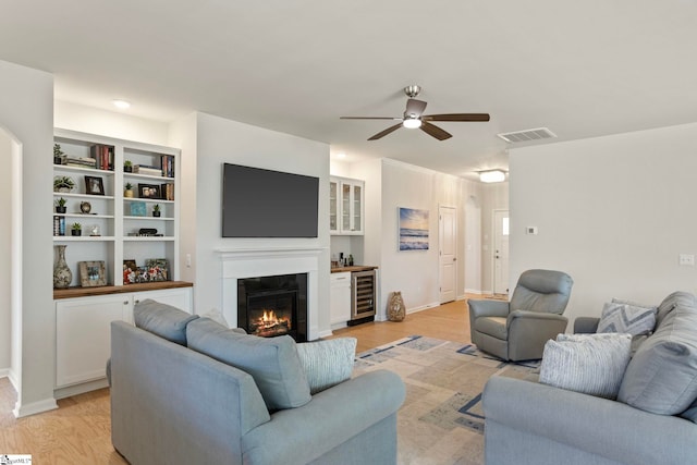 living room with beverage cooler, visible vents, a glass covered fireplace, and light wood-style flooring