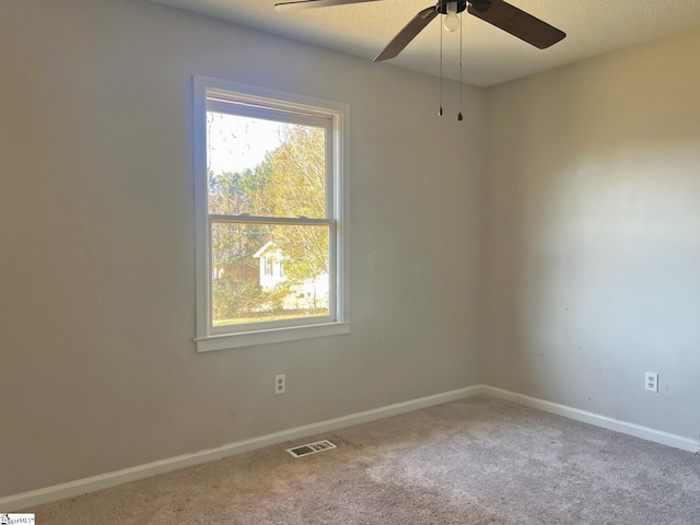 carpeted spare room featuring a ceiling fan, visible vents, and baseboards