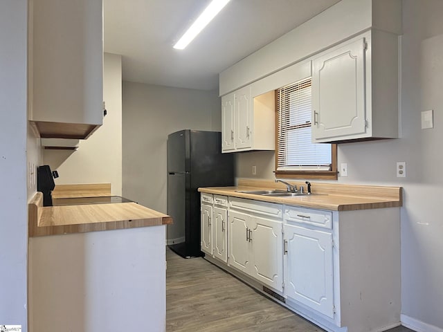 kitchen with wooden counters, stove, white cabinets, a sink, and light wood-type flooring