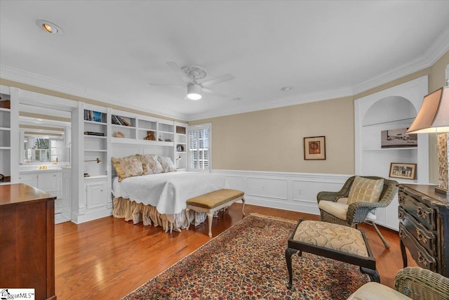 bedroom with ornamental molding, wainscoting, multiple windows, and wood finished floors