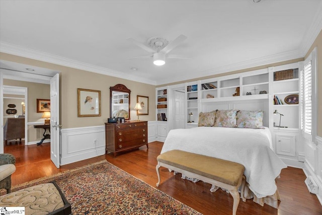 bedroom featuring ornamental molding, a wainscoted wall, a decorative wall, and wood finished floors