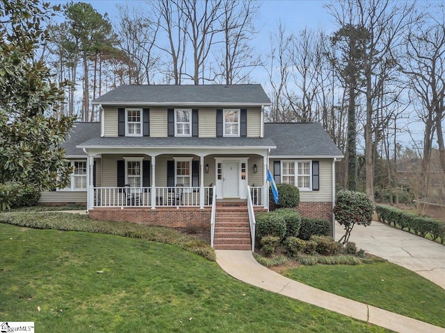 view of front of property with a shingled roof, a front yard, covered porch, and brick siding