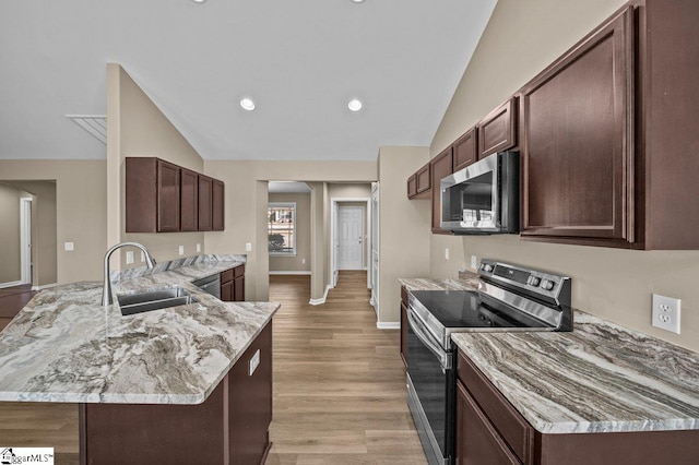 kitchen with light stone counters, appliances with stainless steel finishes, a peninsula, vaulted ceiling, and a sink