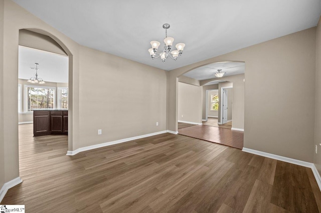 unfurnished room with arched walkways, a notable chandelier, baseboards, and wood finished floors