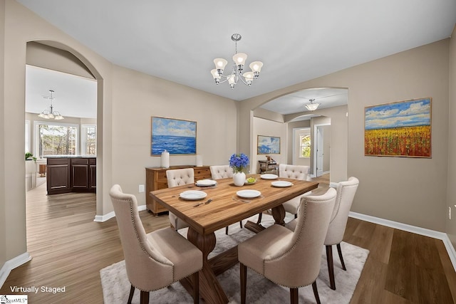 dining room featuring a chandelier, arched walkways, baseboards, and wood finished floors