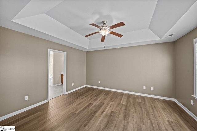 empty room with a tray ceiling, visible vents, baseboards, and wood finished floors